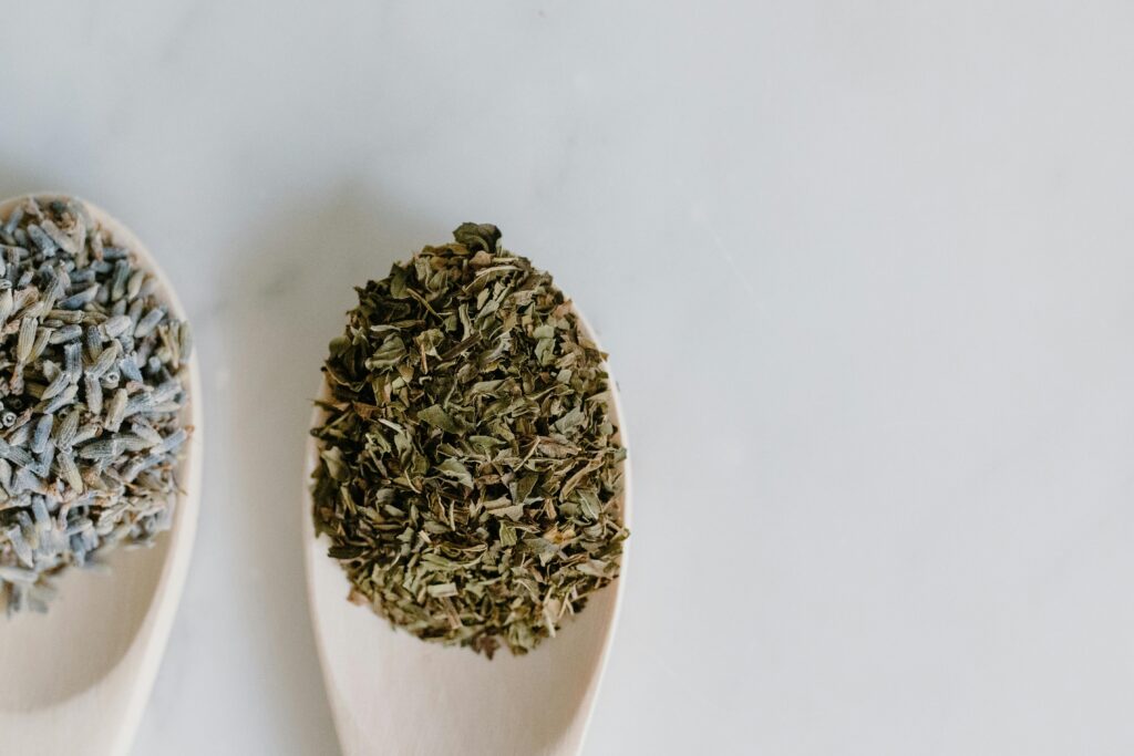 Close-up of dried herbs on wooden spoons against a white background, perfect for culinary use.