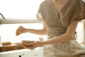 An unrecognizable woman sitting indoors, holding a bowl in soft natural light.